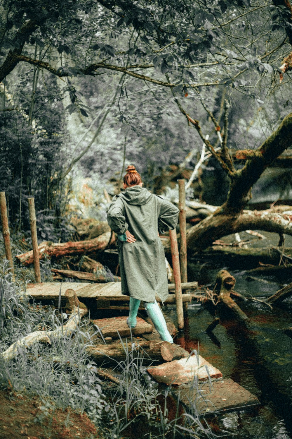 woman in green raincoat walking on footbridge in woods