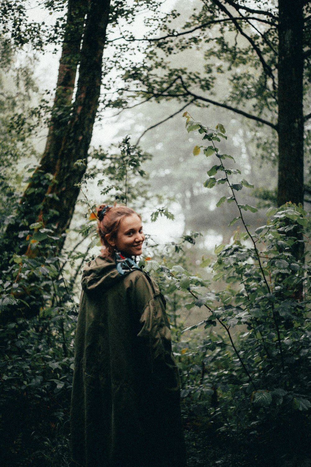 smiling woman in green raincoat standing in woods
