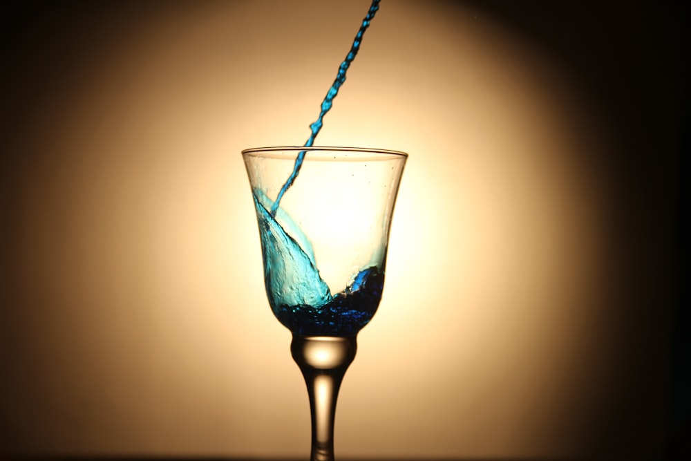 blue liquid pouring on clear footed glass cup