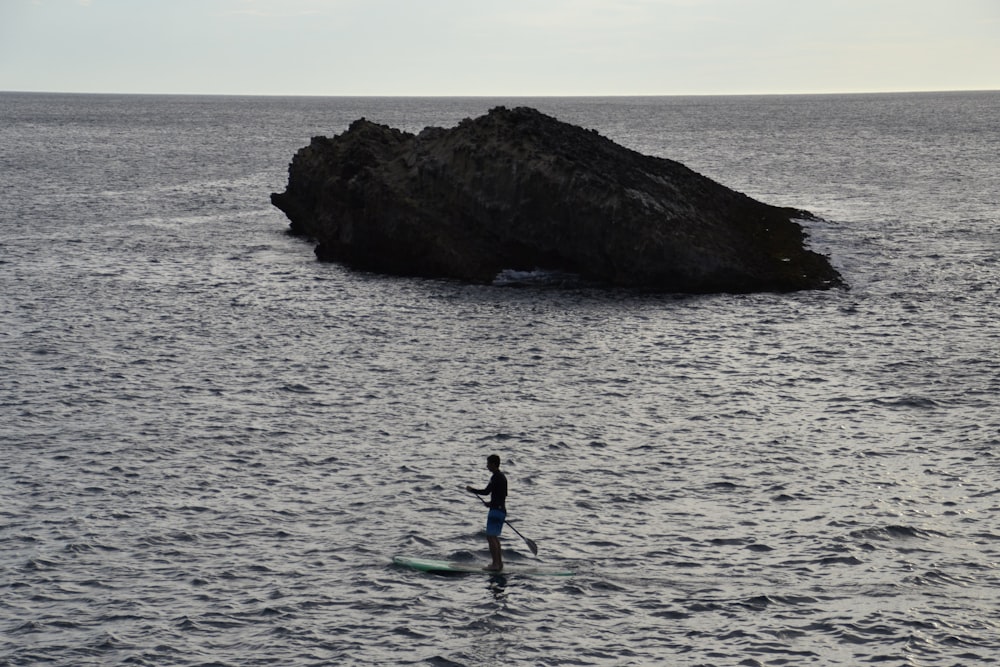 grayscale photography of person paddle boarding