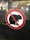 A no-rat symbol is prominently displayed. This sign features a silhouette of a rat with a red circle and a diagonal line across it, indicating prohibition. The background appears to be transparent glass, revealing a blurry view of a store or market environment with various items such as fruits and shelves.
