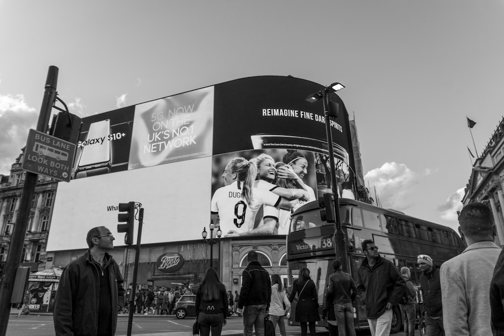 Photographie en niveaux de gris de personnes près d’un bus et d’un bâtiment