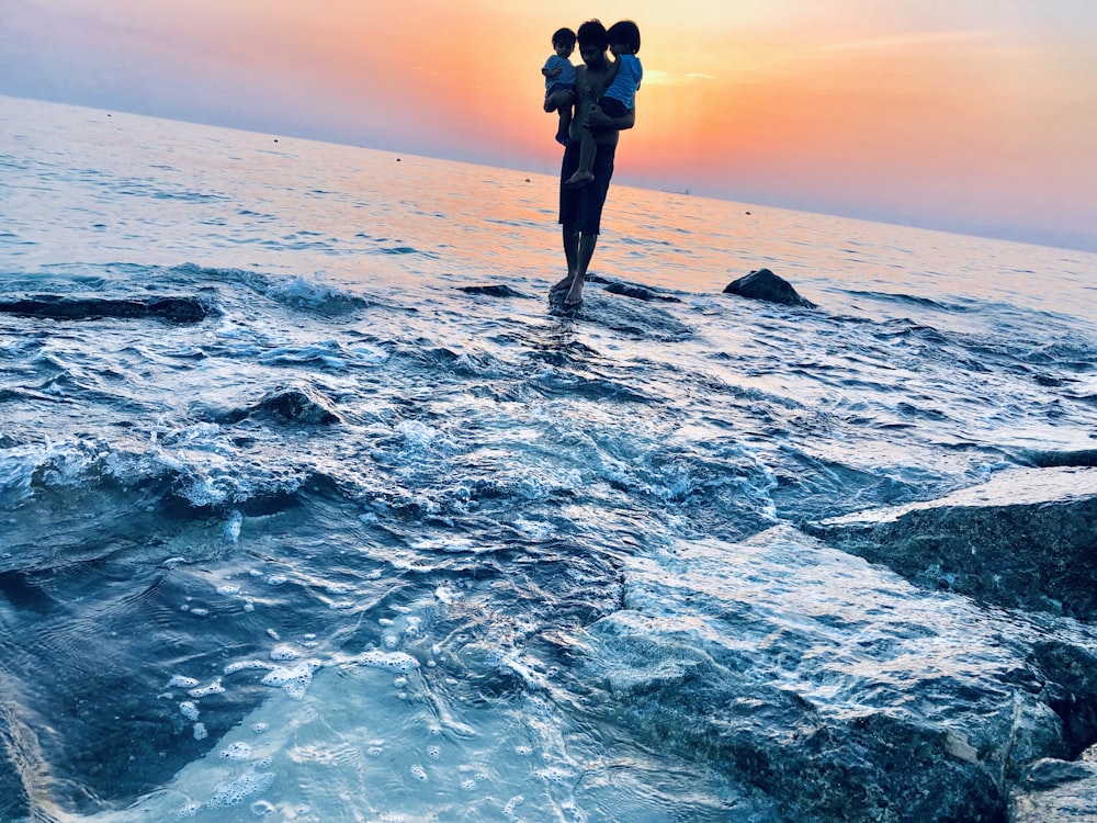 man standing on rock formation while carrying two children during daytime