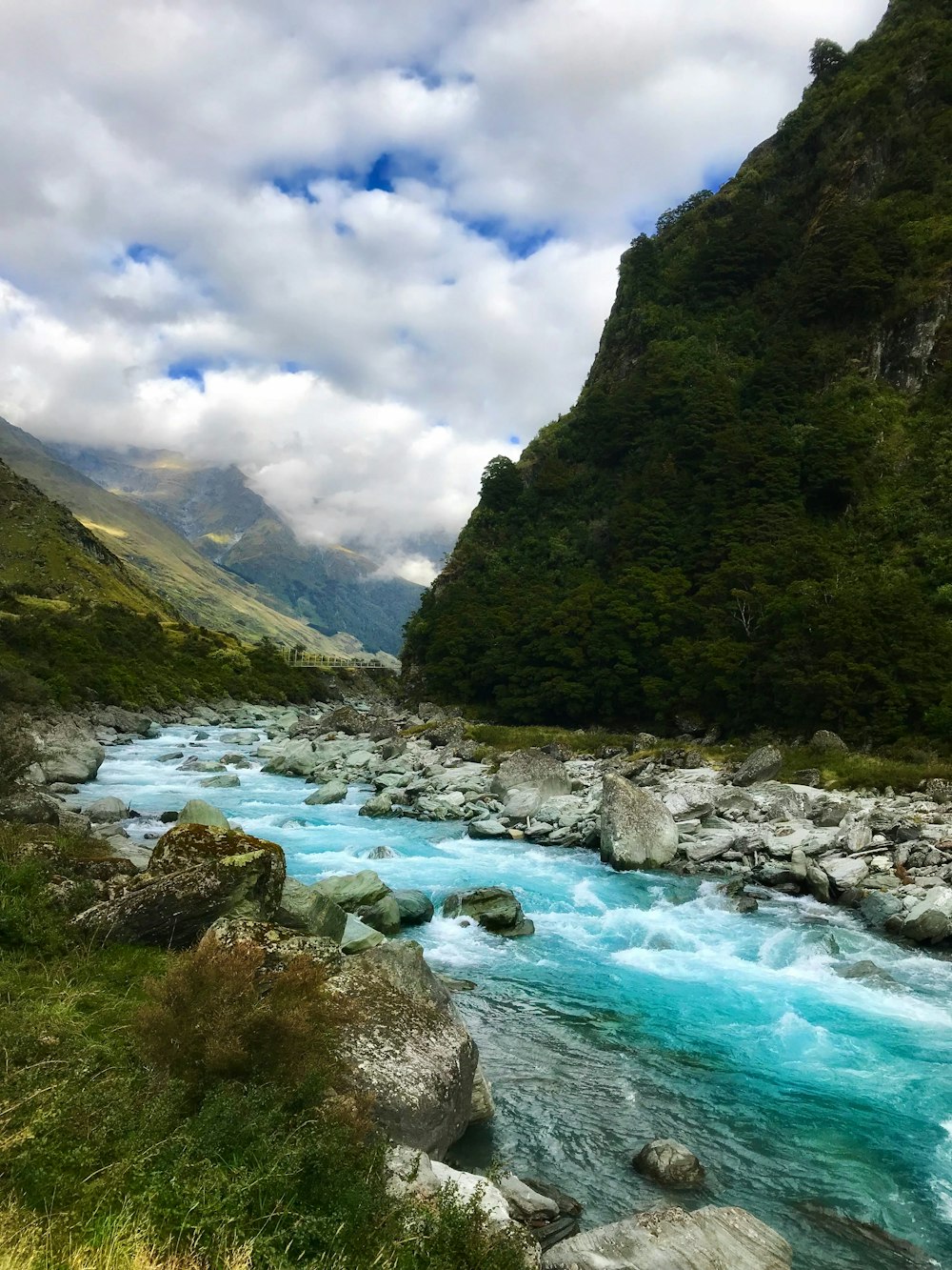 Río que fluye cerca de la montaña verde bajo nubes blancas