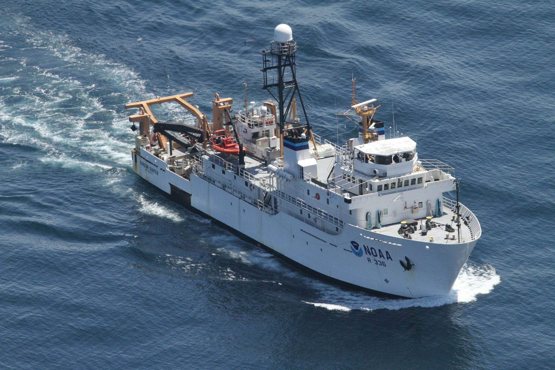 A large research vessel navigates through the ocean, leaving a trail of white foam in its wake. The ship is equipped with various antennas and cranes, highlighting its function for scientific exploration. The vessel's name and identification number are visible on its side.