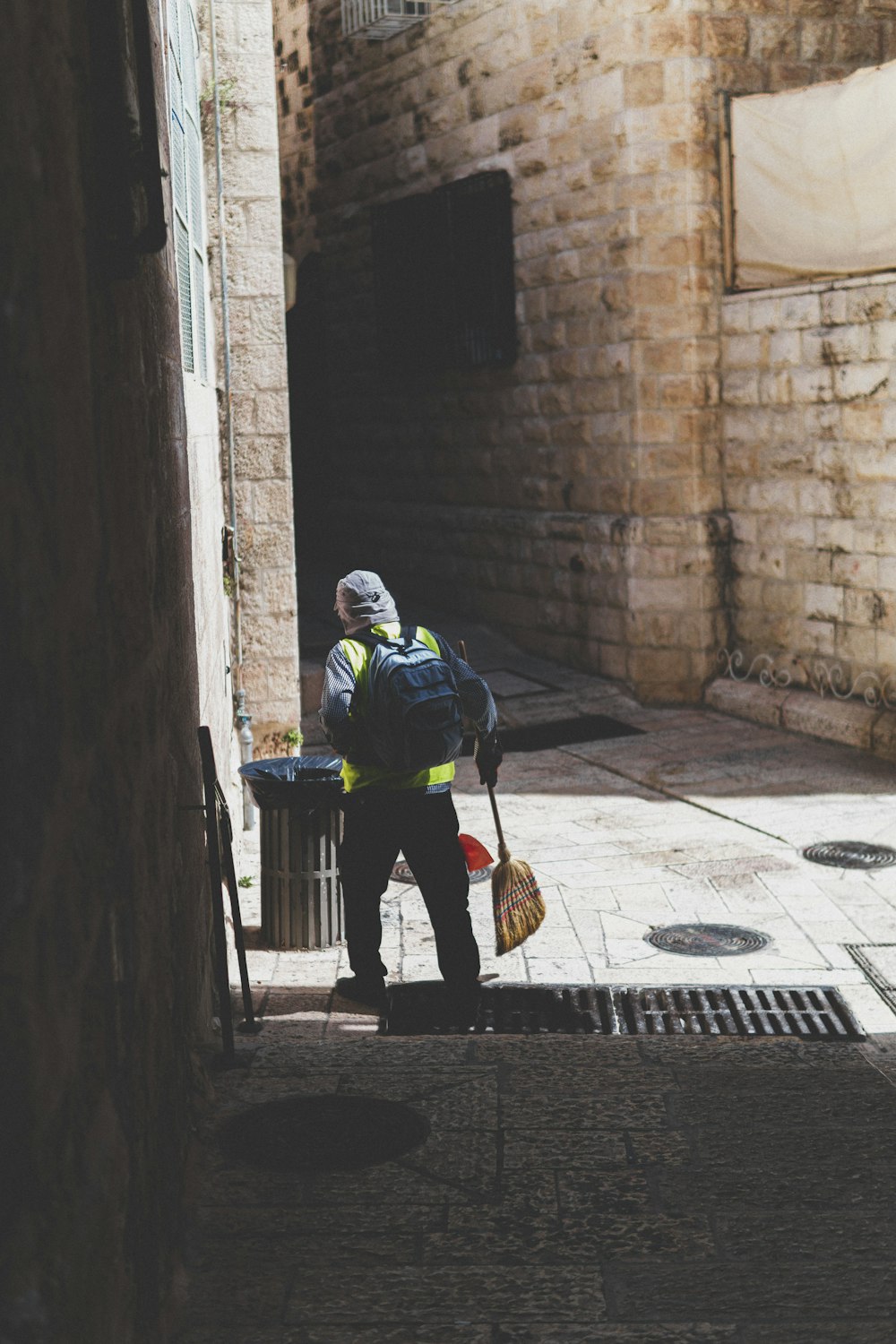 person holding brown broomstick besides gray bin