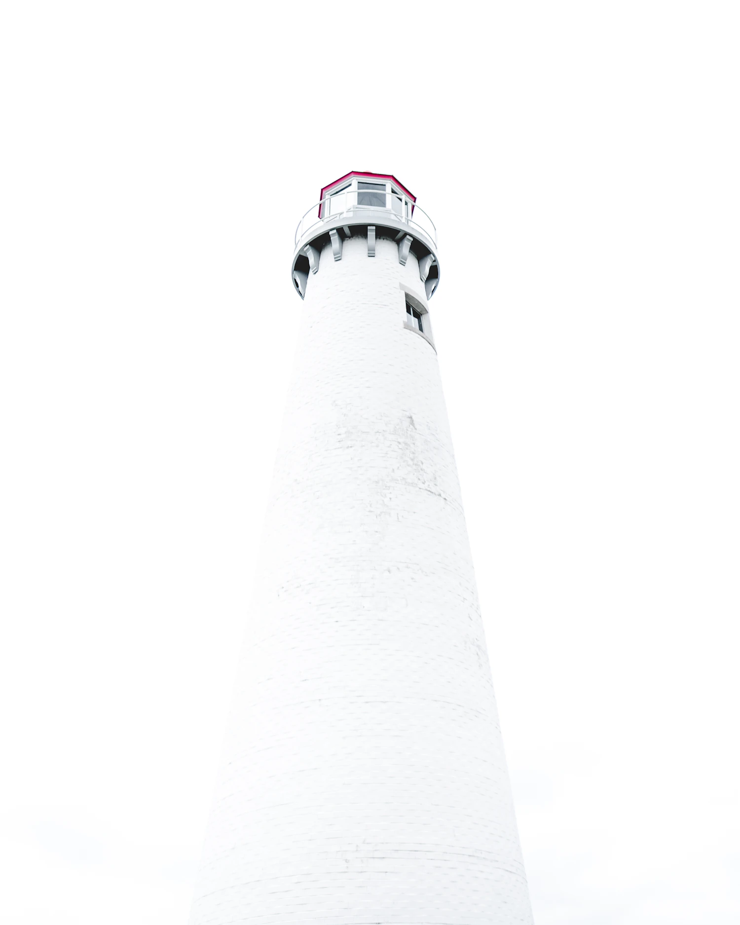 A white lighthouse tower seen from below against a blank white sky