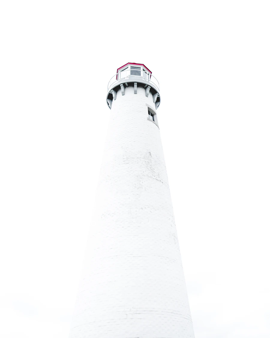 A white lighthouse tower seen from below against a blank white sky