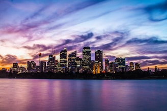 lighted city buildings near body of water under cloudy sky