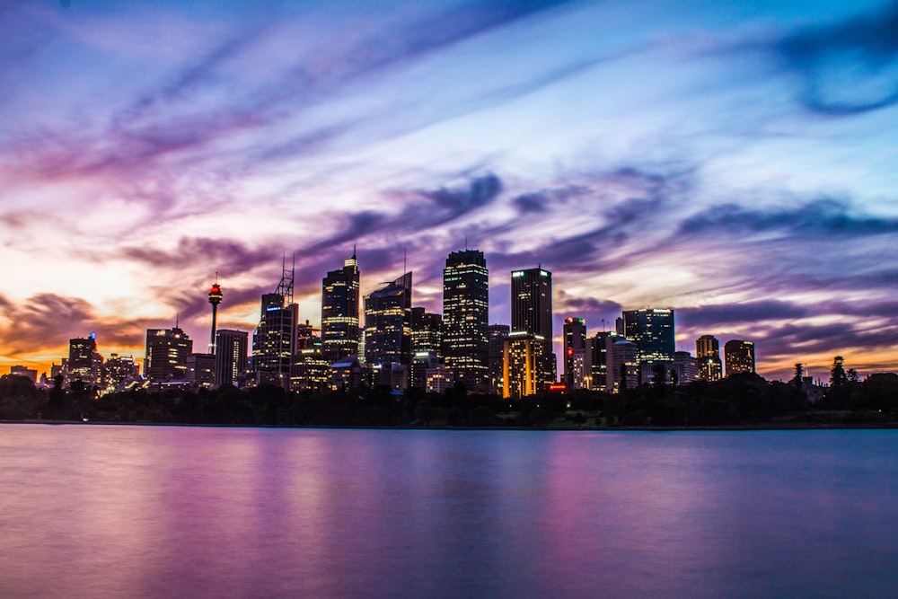 lighted city buildings near body of water under cloudy sky