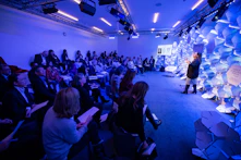 woman making speech in front of people sitting on individual chairs