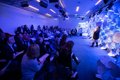 woman making speech in front of people sitting on individual chairs