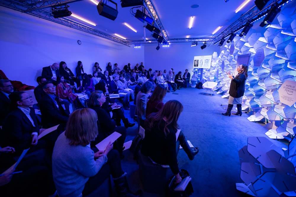 woman making speech in front of people sitting on individual chairs