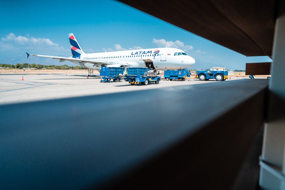 blue trucks near white and blue Latam airplane on railway