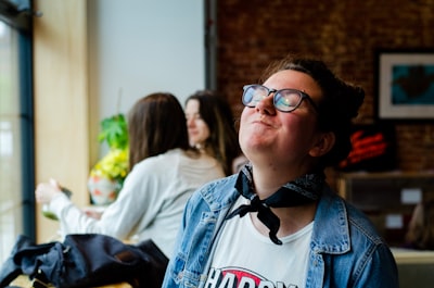 woman wearing blue denim jacket sitting and smiling while closing her eyes eat teams background