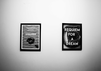 Two framed posters are displayed on a plain white wall. The left poster features the title 'STALKER' along with other text and an image resembling a rock or artifact in sand. The right poster is titled 'REQUIEM FOR A DREAM' and features a close-up of an eye or a circular design.