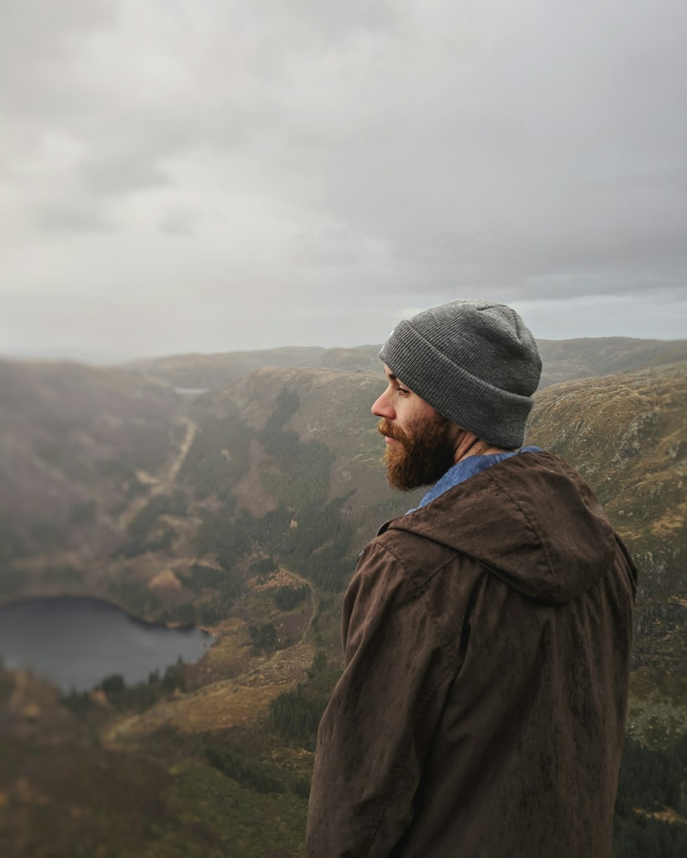 man standing and facing on lake and mountain