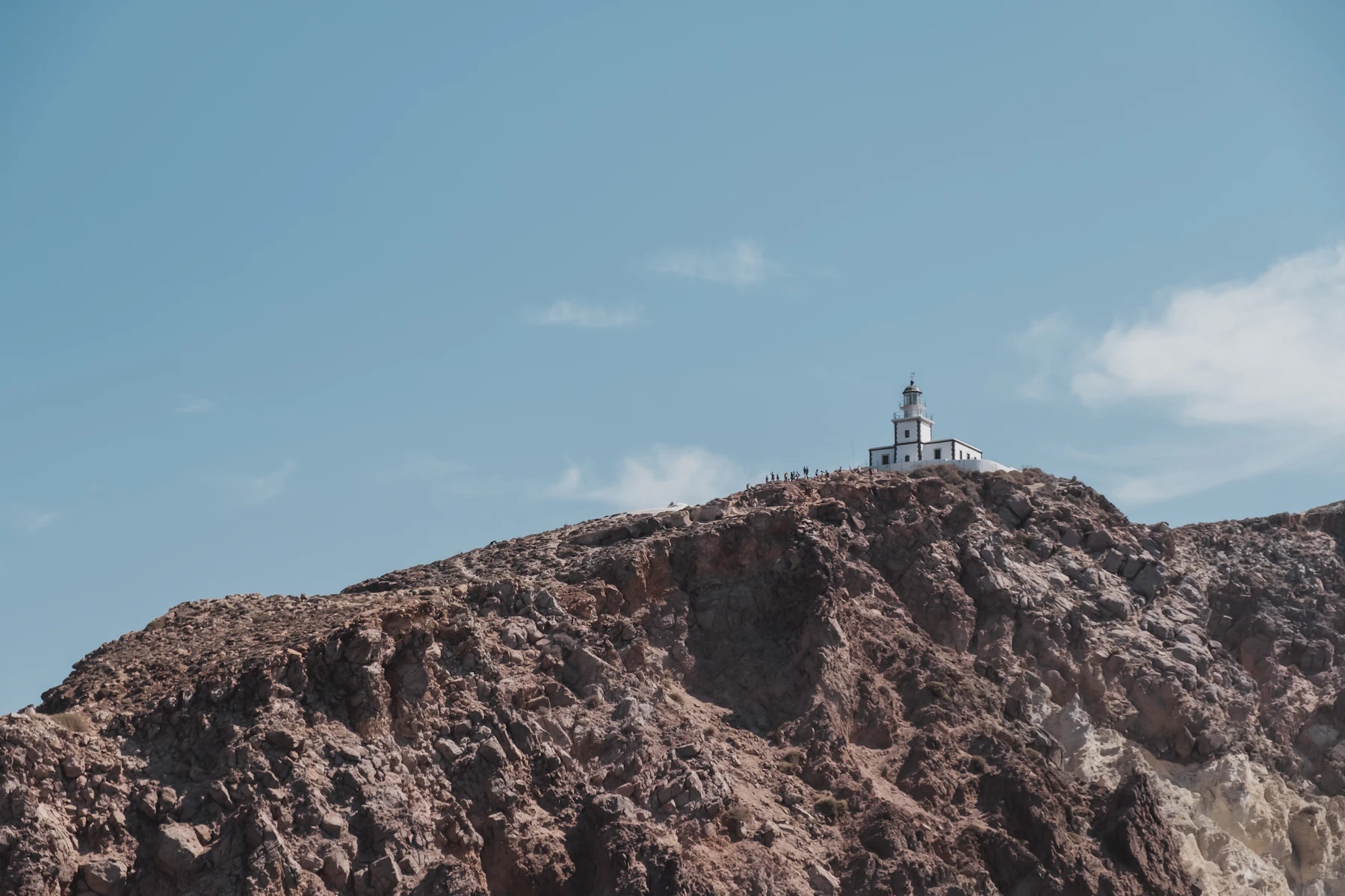 A small white lighthouse standing on a bare, sun-bleached rocky headland against a pale sky.