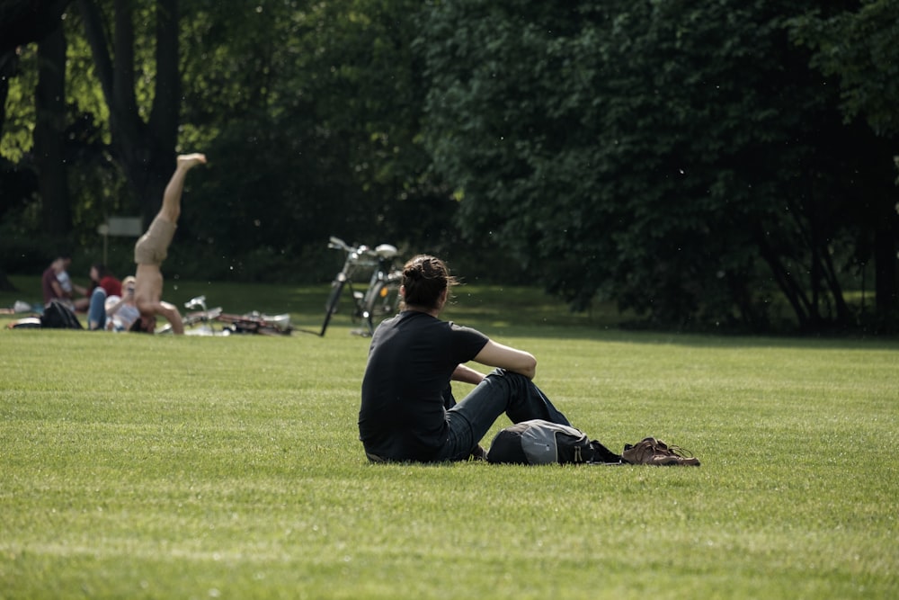 man in black t-shirt and blue denim jeans sitting on green grass in field