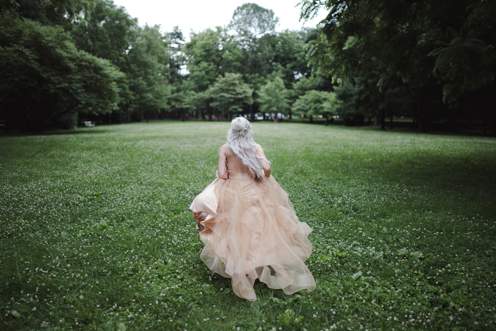 woman walking on grass field surrounded with trees