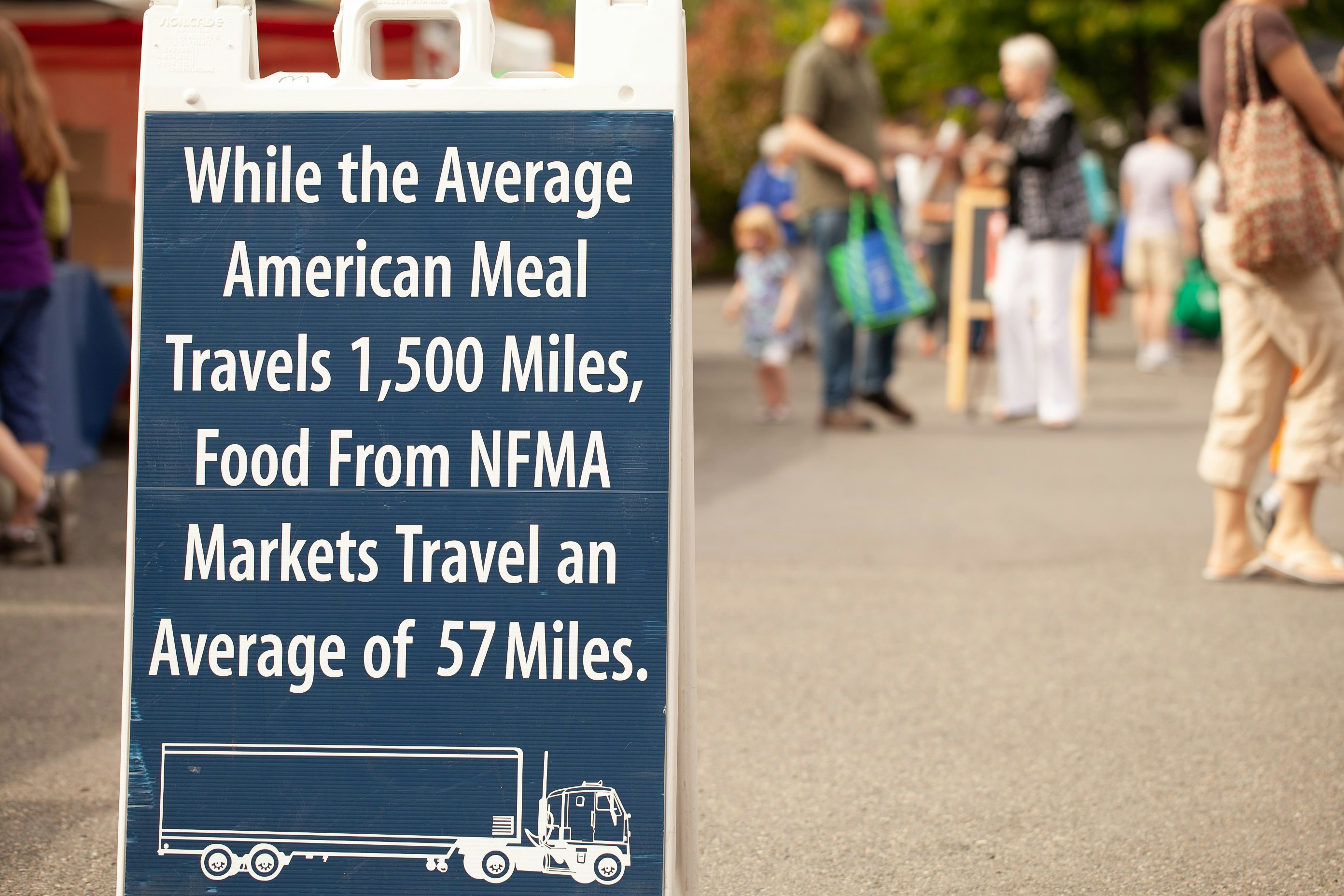 people standing near road with road sign saying while the average American meal travels 1,500 miles, food from NFMA markets travel an average of 57 miles