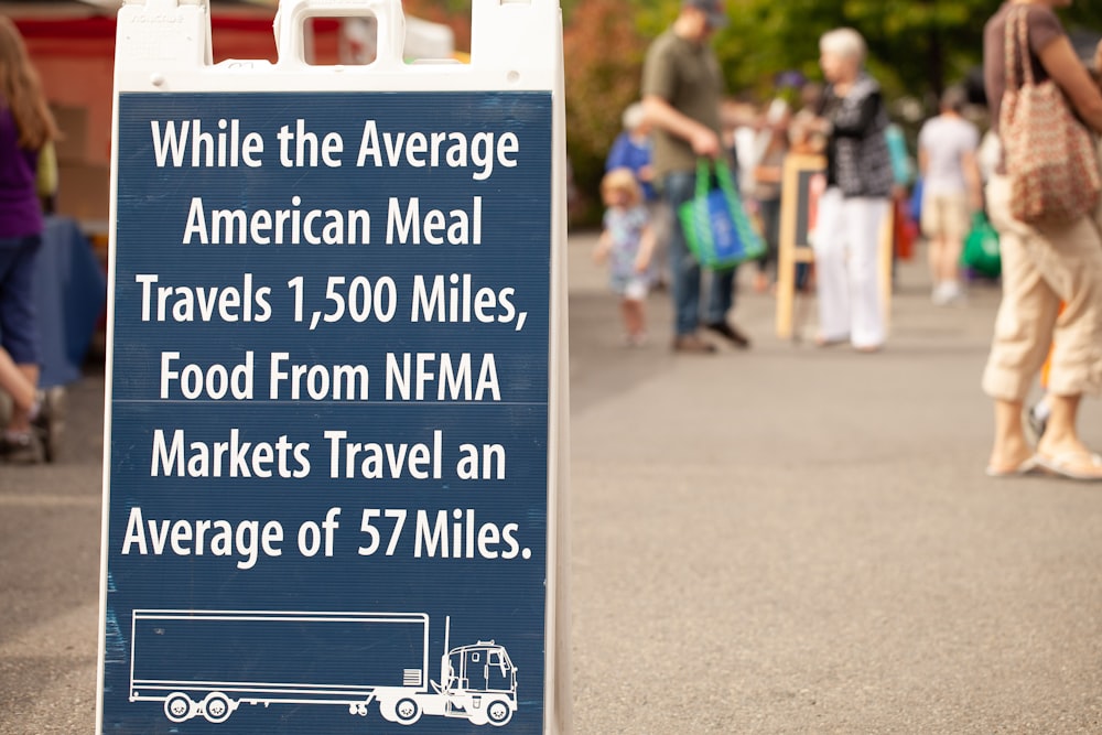 people standing near road with road sign saying while the average American meal travels 1,500 miles, food from NFMA markets travel an average of 57 miles