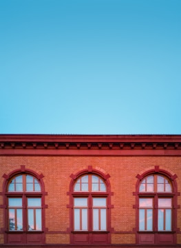 red and brown concrete building with three glass windows under blue sky