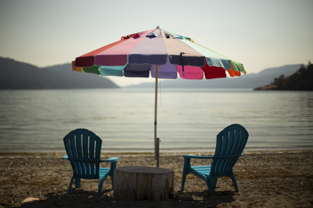 two blue lounge chairs under multicolored parasol in beach