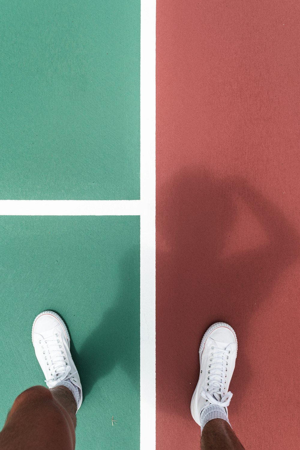 person wearing white sneakers standing on between green and red pavement