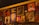 A wall adorned with various pieces of artwork, showcasing diverse styles and subjects. The artwork includes abstract designs, portraits, and graphic typography. Below the artworks, bottles are arranged, suggesting it might be a bar or café setting.