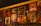 A wall adorned with various pieces of artwork, showcasing diverse styles and subjects. The artwork includes abstract designs, portraits, and graphic typography. Below the artworks, bottles are arranged, suggesting it might be a bar or café setting.