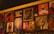 A wall adorned with various pieces of artwork, showcasing diverse styles and subjects. The artwork includes abstract designs, portraits, and graphic typography. Below the artworks, bottles are arranged, suggesting it might be a bar or café setting.