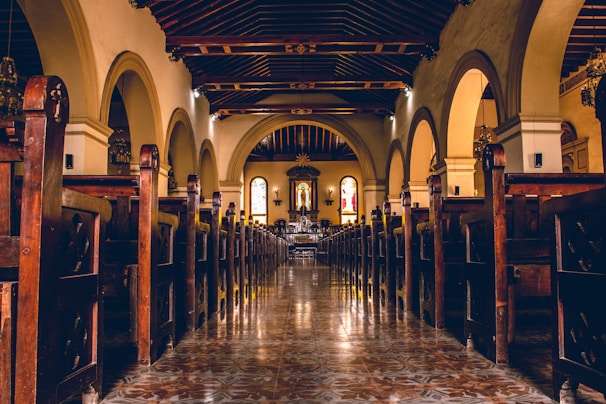 Interior view of a sunlit church aisle lined with wooden pews and soft floral arrangements.