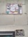 A wall featuring a large sign covered with a variety of graffiti stickers and tags. The stickers have diverse styles, including logos and hand-drawn elements. Below this, a smaller sign exhibits more graffiti writing in black paint, creating an urban and gritty aesthetic.