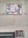 A wall featuring a large sign covered with a variety of graffiti stickers and tags. The stickers have diverse styles, including logos and hand-drawn elements. Below this, a smaller sign exhibits more graffiti writing in black paint, creating an urban and gritty aesthetic.