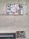 A wall featuring a large sign covered with a variety of graffiti stickers and tags. The stickers have diverse styles, including logos and hand-drawn elements. Below this, a smaller sign exhibits more graffiti writing in black paint, creating an urban and gritty aesthetic.