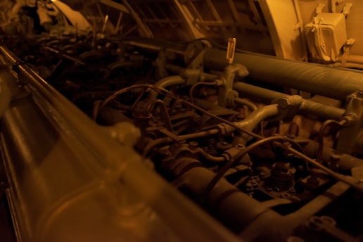 A complex array of machinery parts, including pipes, tubes, and valves, illuminated in a dim, warm light. The setting appears industrial, with metallic and mechanical components arranged within a confined space.