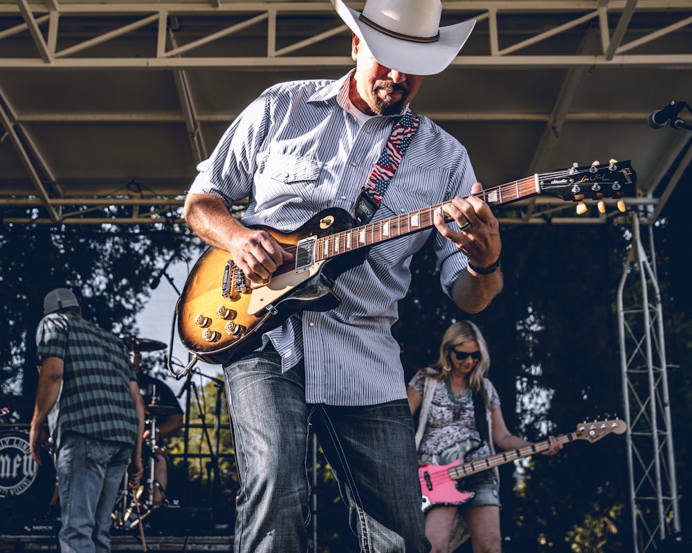 Homem de camisa branca e azul listrada de mangas compridas tocando guitarra elétrica no palco