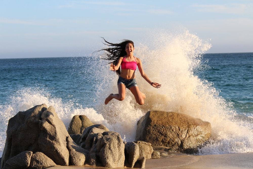 woman jumping on rocky shore at daytime