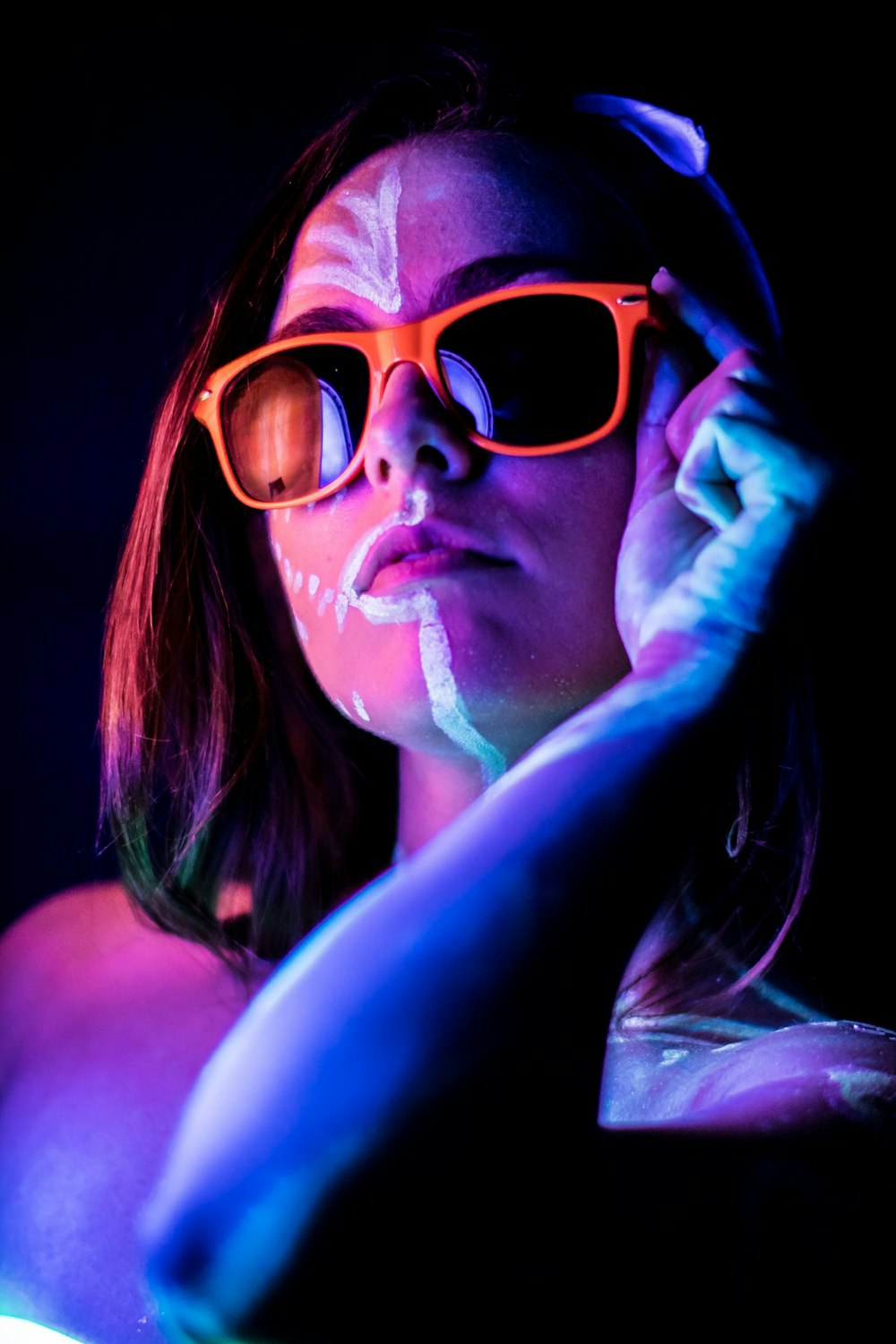 Frau mit orangefarbener Sonnenbrille mit Farbe im Gesicht