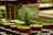 A cluster of small, red pots containing young green plants arranged on industrial metal shelves. The lighting highlights the vibrant greenery and the smooth texture of the pots. In the center, a taller plant stands out, suggesting a rosemary or similar herb.