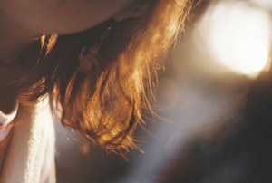 A close-up shot of a person's hair with sunlight creating a warm, golden glow. The soft focus adds to a dreamy atmosphere, highlighting the subtle textures of the hair as it catches the light.