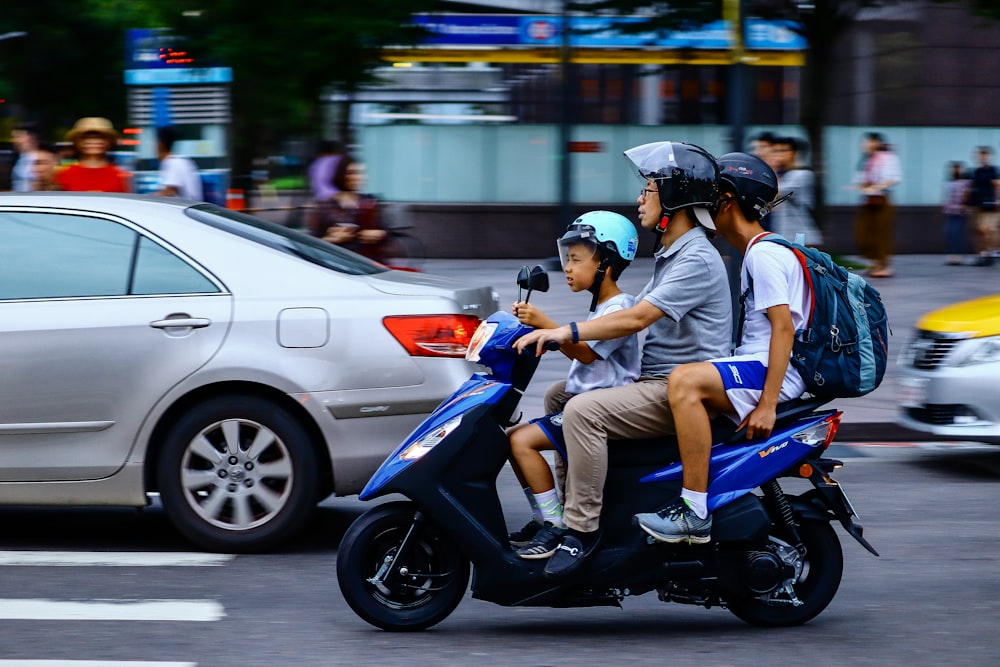 three people riding blue motor scooter