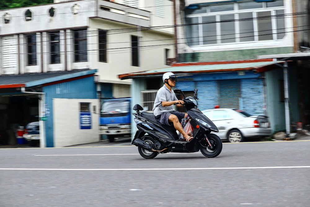 man riding motor scooter on road near cars and buildings