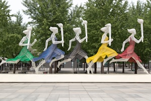 five running women wearing different dresses holding torch statue