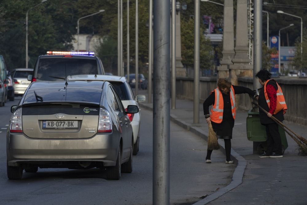 two woman holding broom sticks beside vehicles