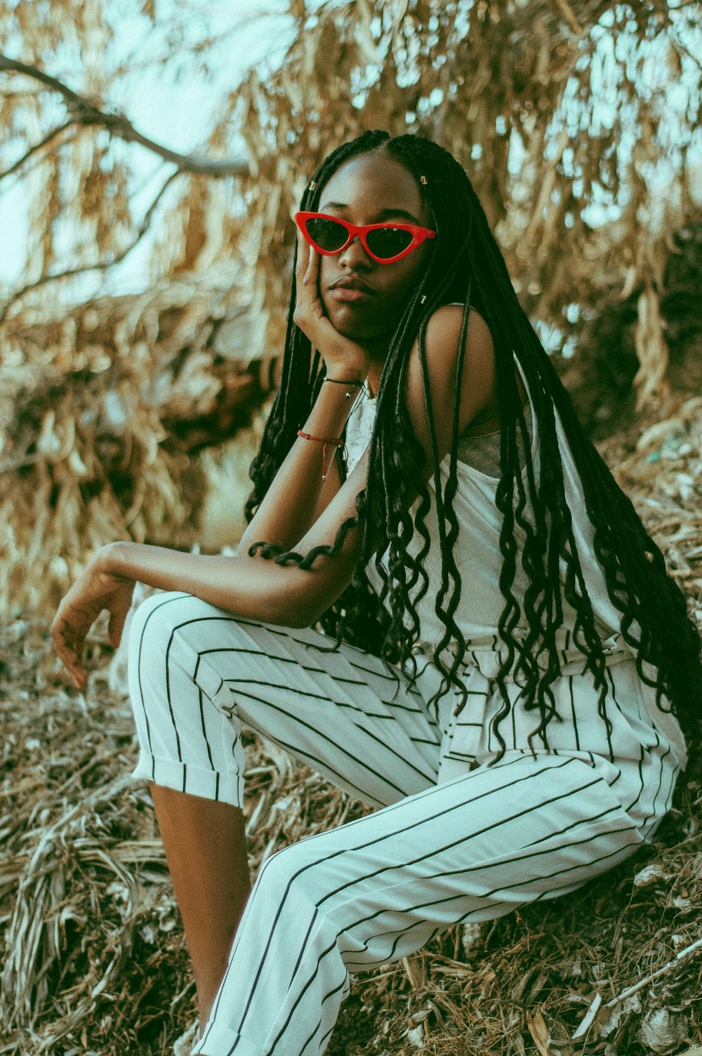 woman wears red sunglasses, white sleeveless top and white-and-black striped pants