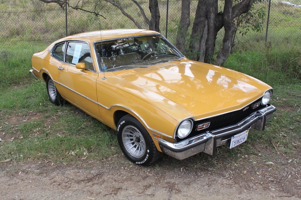 yellow classic coupe parked beside tree