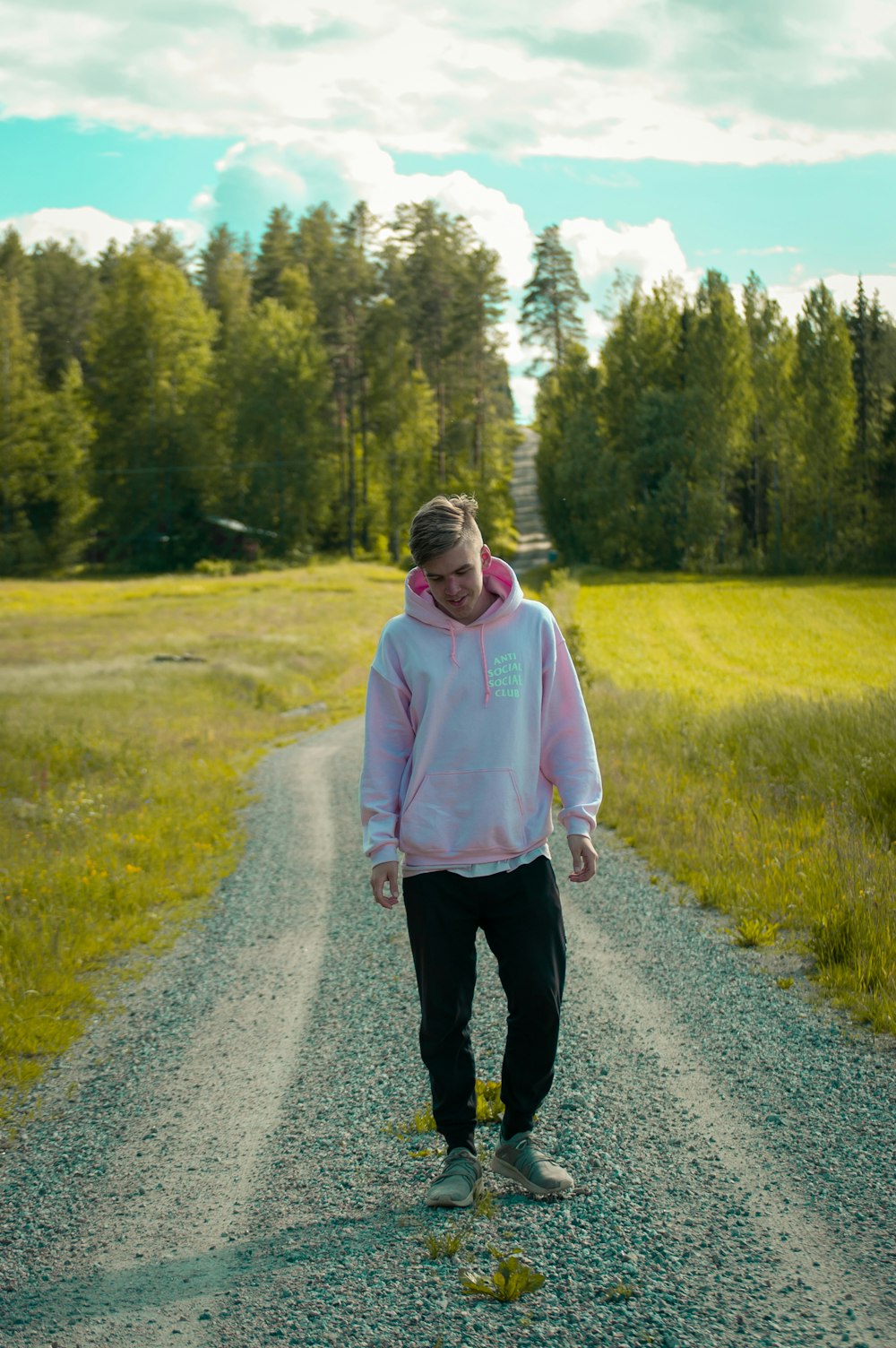 man with pink hoodie standing on the road between green grass