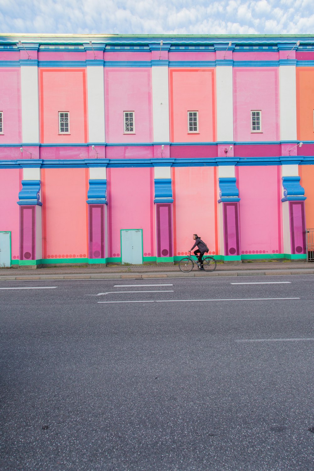 person driving a bike near multi-colored building during daytime